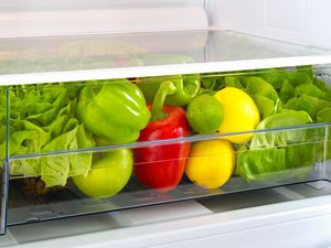 Vegetables and fruits in a refrigerator crisper drawer including lettuce bell peppers and citrus fruits
