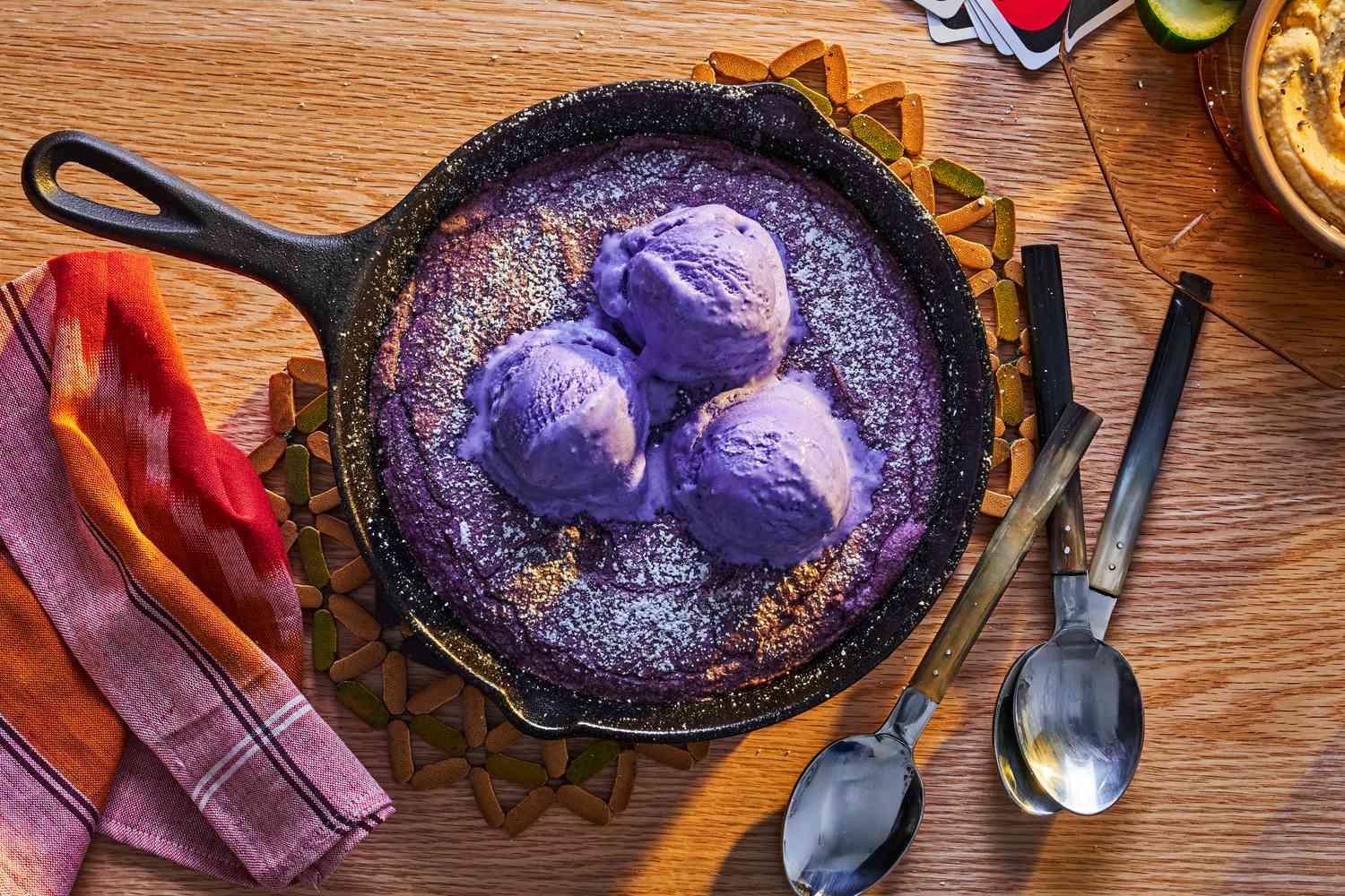 Ube skillet cookie topped with ube ice cream, spoons alongside