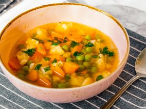 Bowl of vegetable soup with carrots peas and herbs on a striped cloth