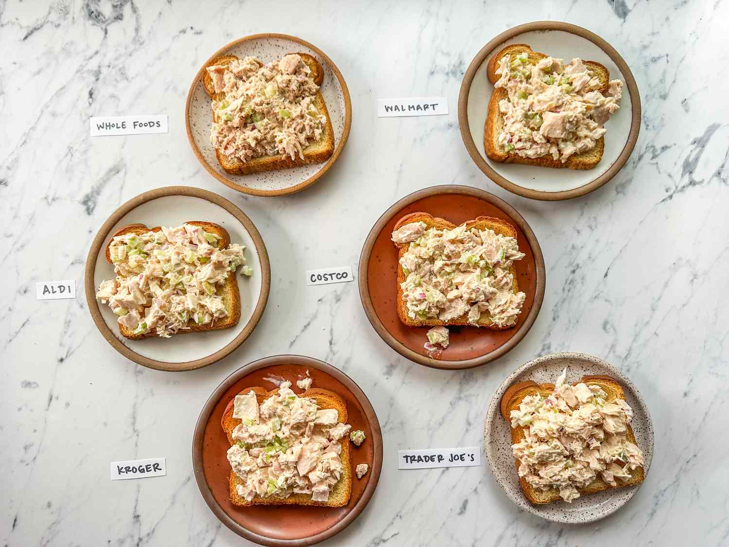 Six plates of tuna salad toasts labeled with store names for comparison