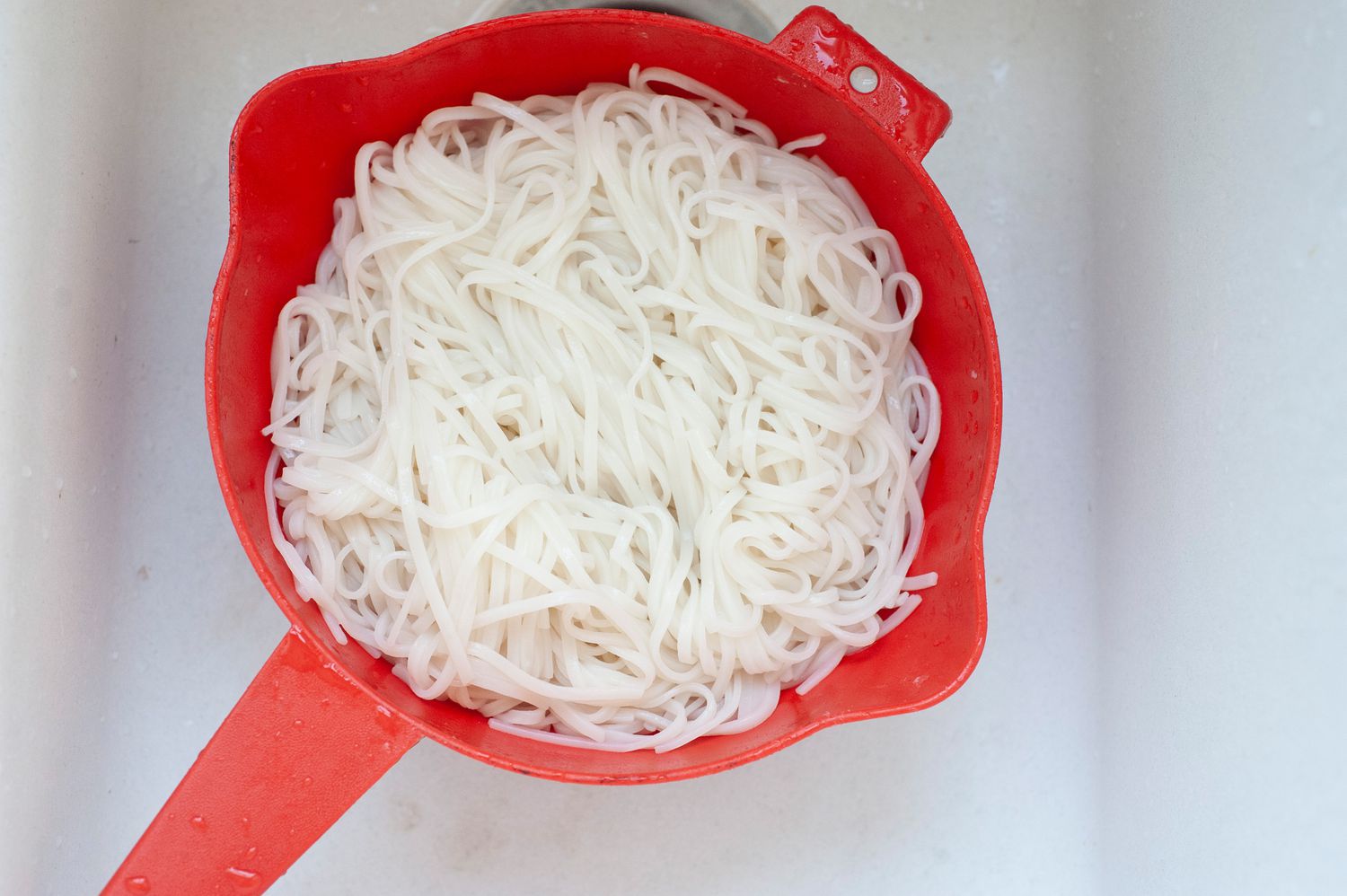Draining rice noodles to make a vegetarian rice noodle salad.