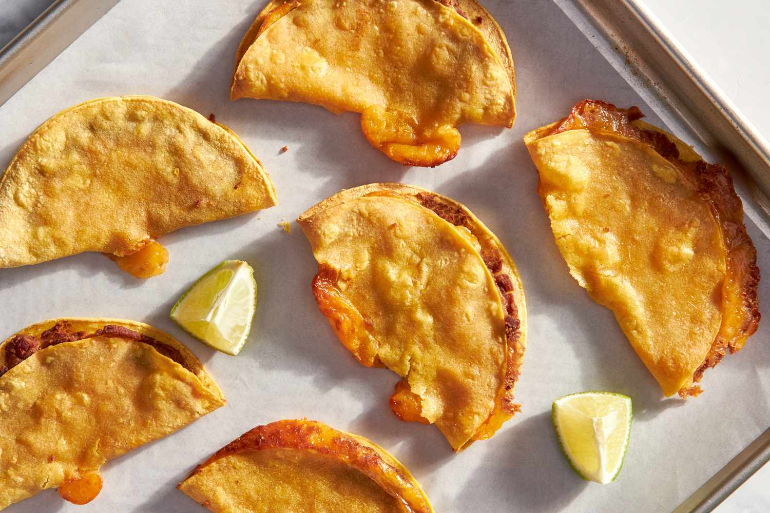 Cheesy baked tacos on a parchment paper lined baking sheet with lime wedges
