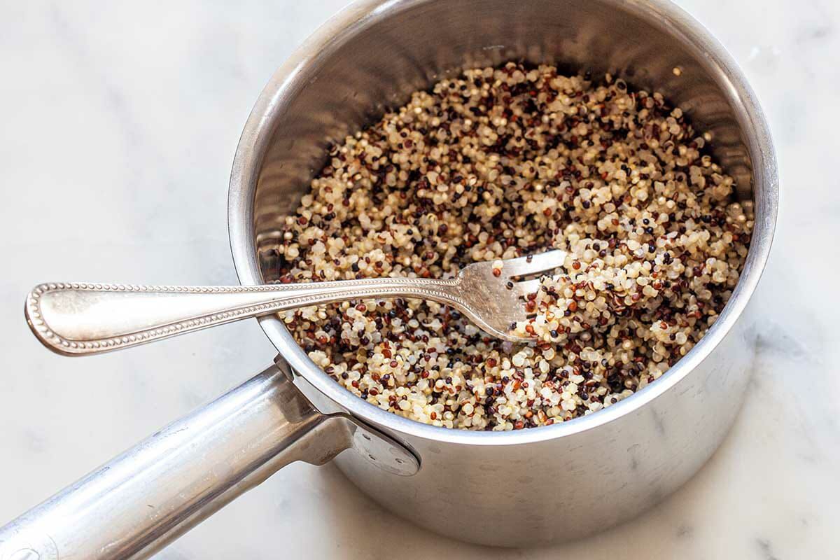 A saucepan of perfect quinoa and a large serving fork to show how to cook fluffy quinoa.