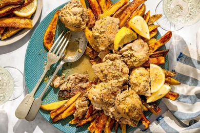 A dish of braised chicken served on a plate with fries and lemon wedges