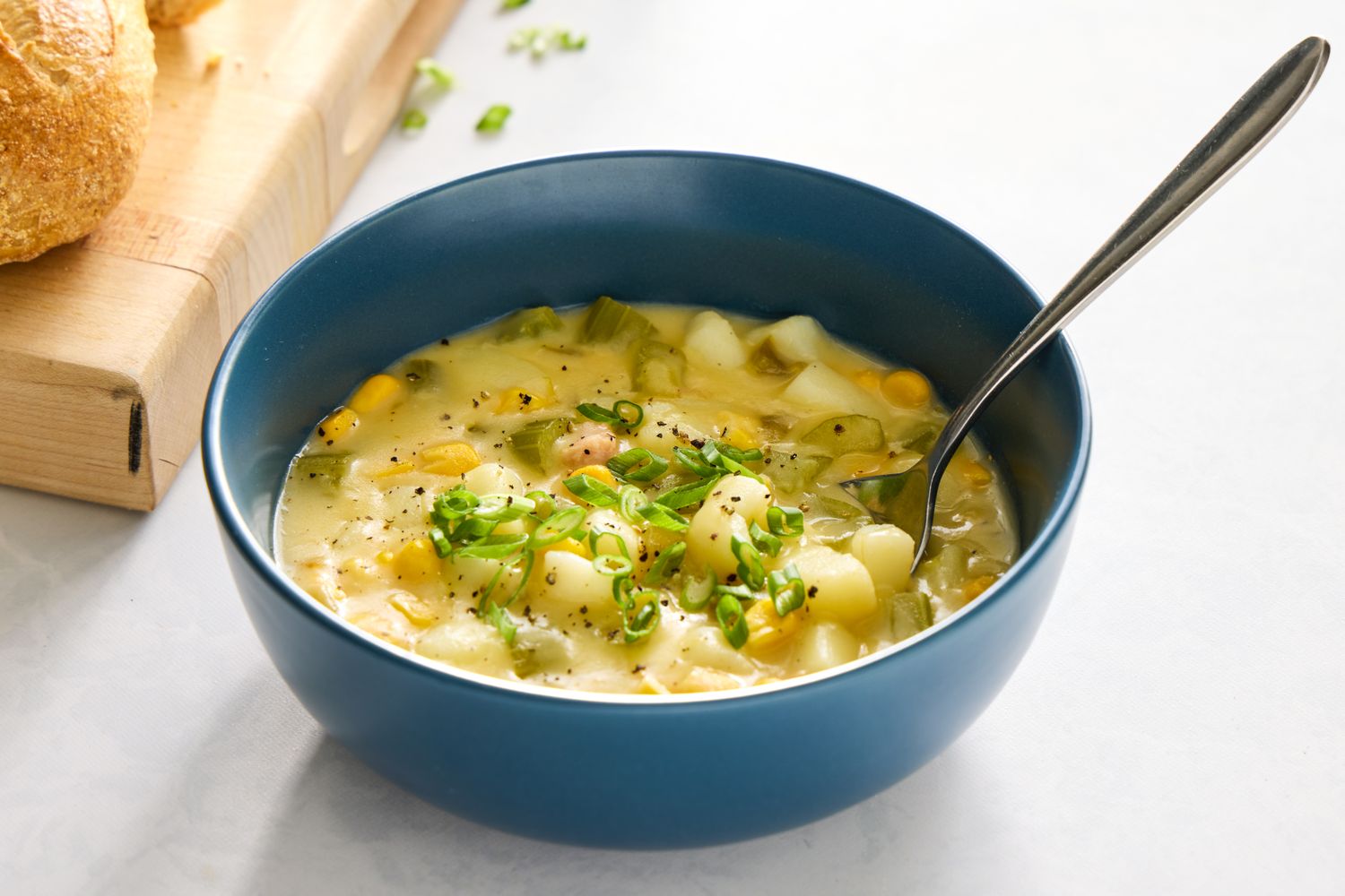A bowl of chicken corn chowder topped with green onions served with bread nearby