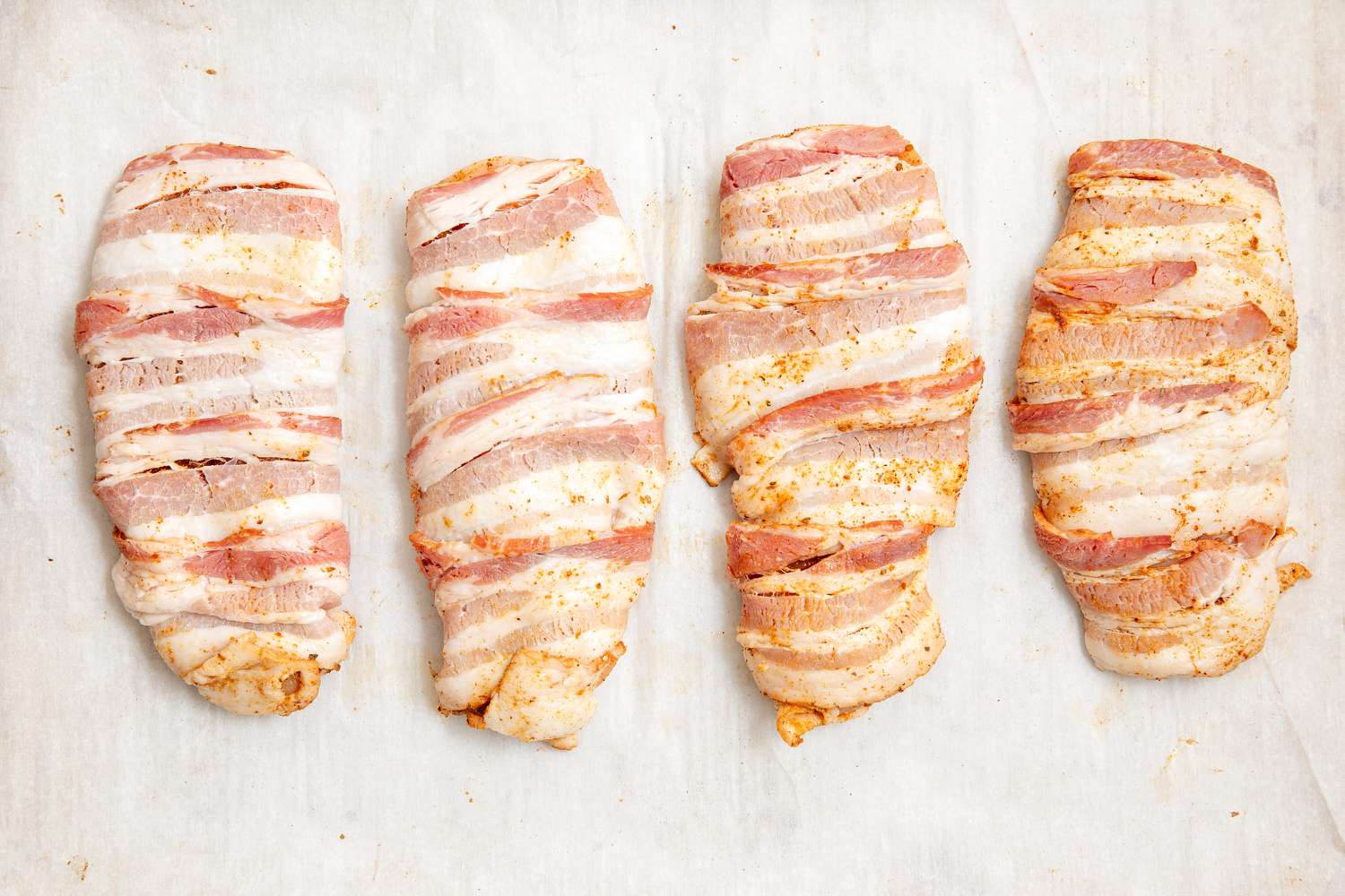 bacon wrapped around chicken breast pieces and seasoned; on parchment for Bacon-Wrapped Chicken