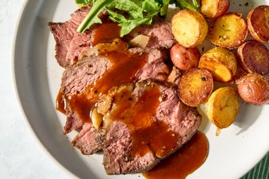 Sliced roast beef with gravy accompanied by roasted potatoes and greens on a plate