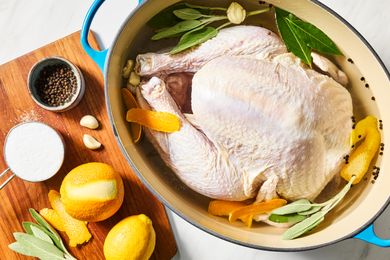 A raw turkey in a pot with herbs, citrus, spices, and brine