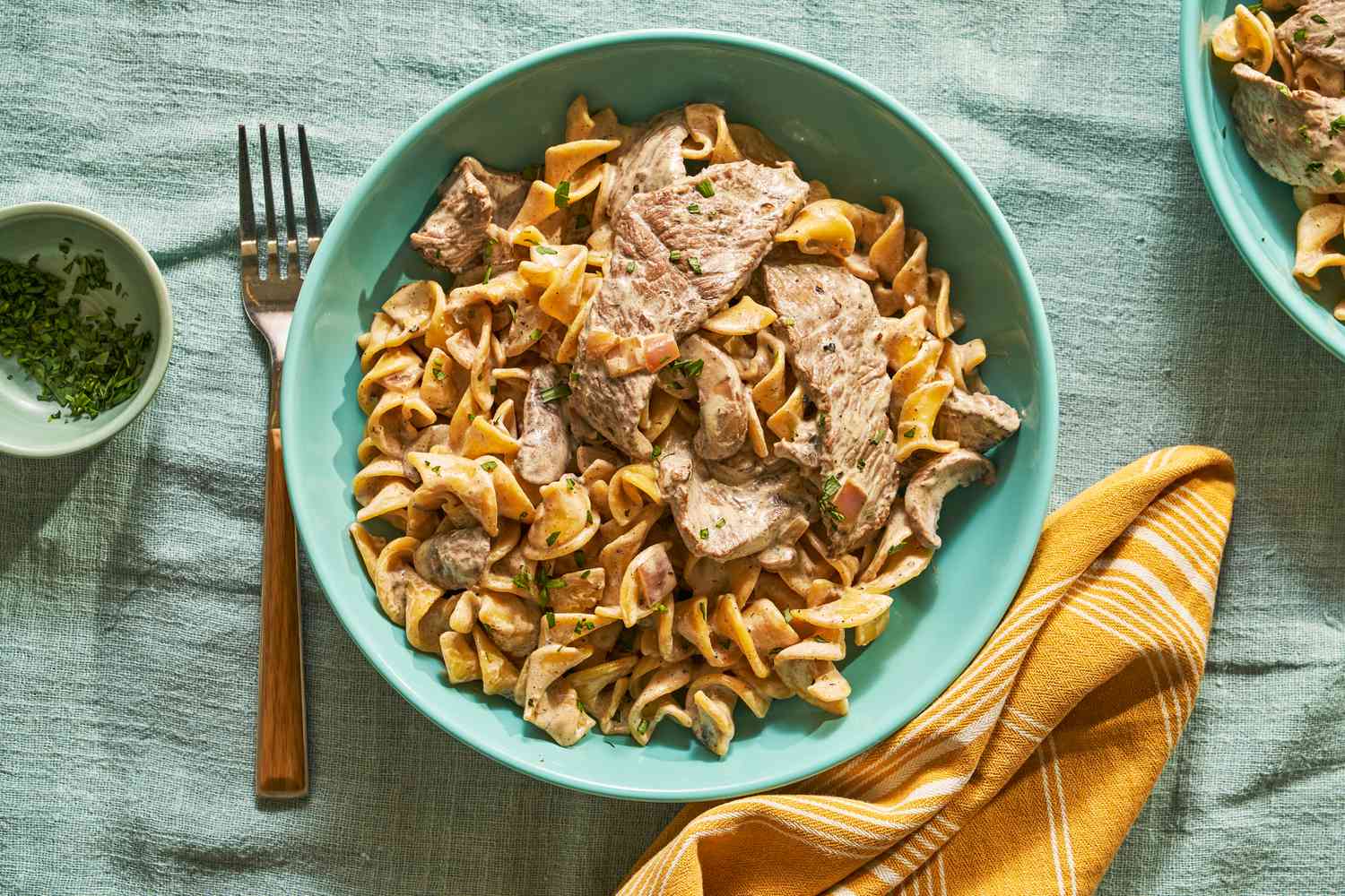 A shallow bowl of beef Stroganoff over pasta on a dinner table 