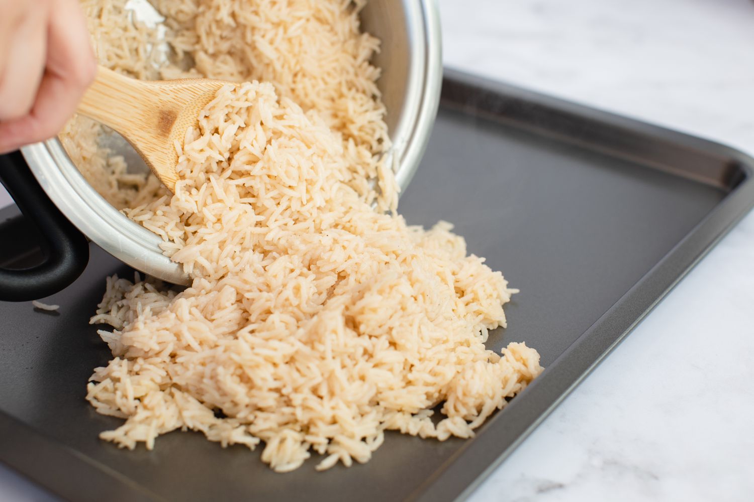 Spooning rice onto a sheet pan to make a dirty rice recipe.