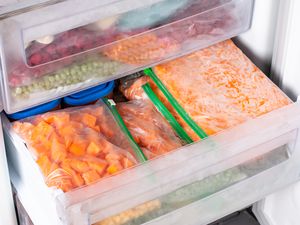 Angled view of one open and one closed freezer drawer stacked full of various frozen fruits and vegetables in plastic zipper style storage bags