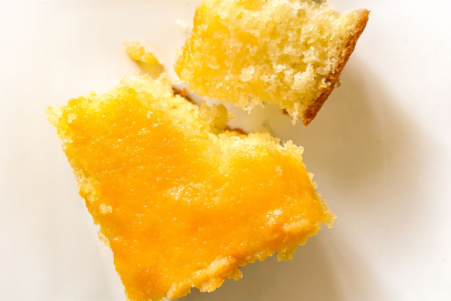 A sliced piece of cake with a bright yellow topping closeup showing texture and detail - Mary Berry’s Lemon Drizzle Traybake Cake