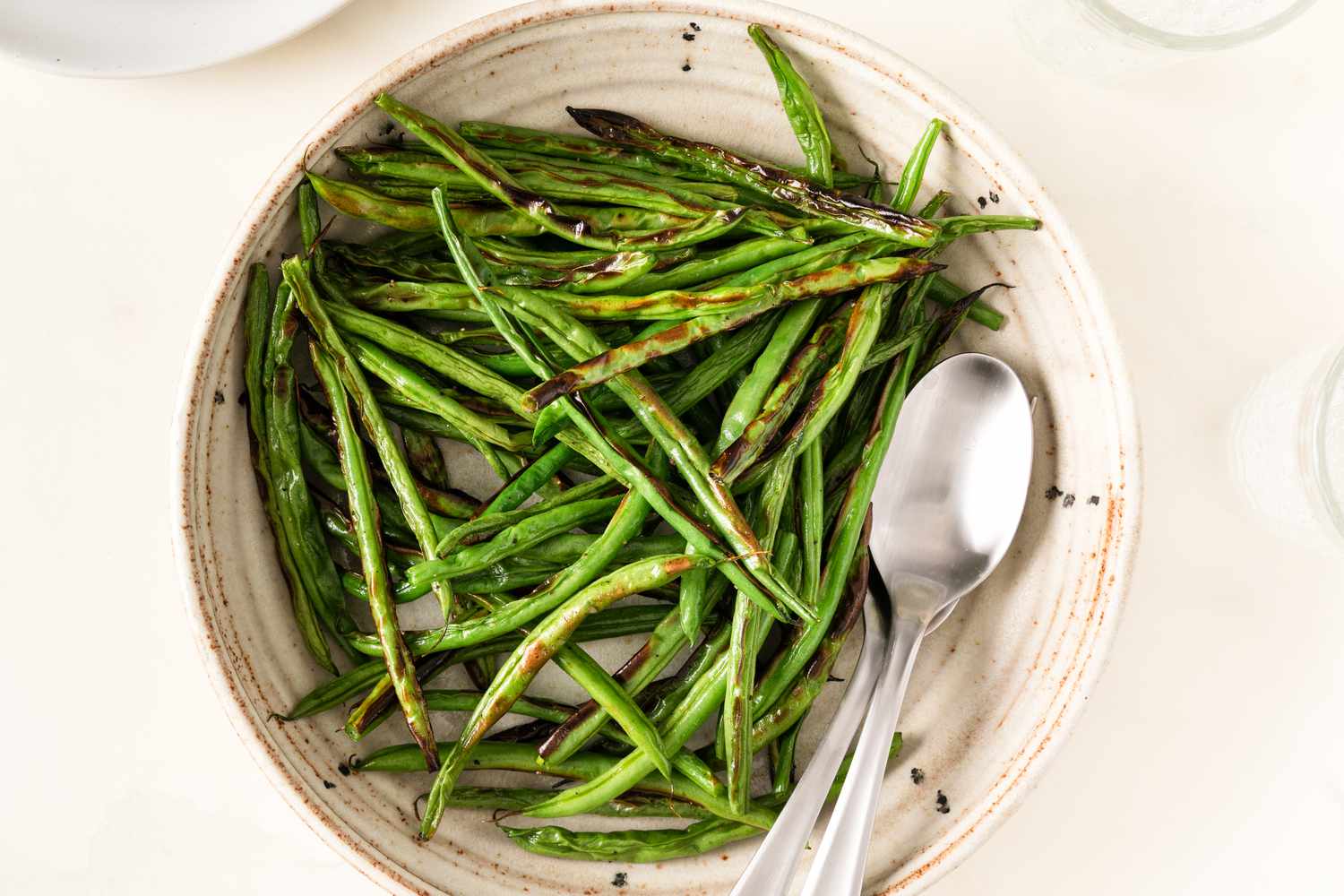 A bowl containing broiled green beans with a spoon and fork