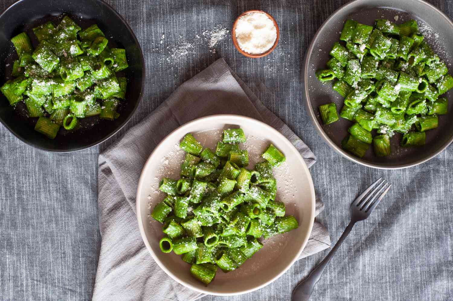 Overhead view of three bowls of simple pasta with green sauce