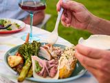 Plate of food being served with Alabama white sauce, including vegetables and meats, a dining setup in an outdoor setting