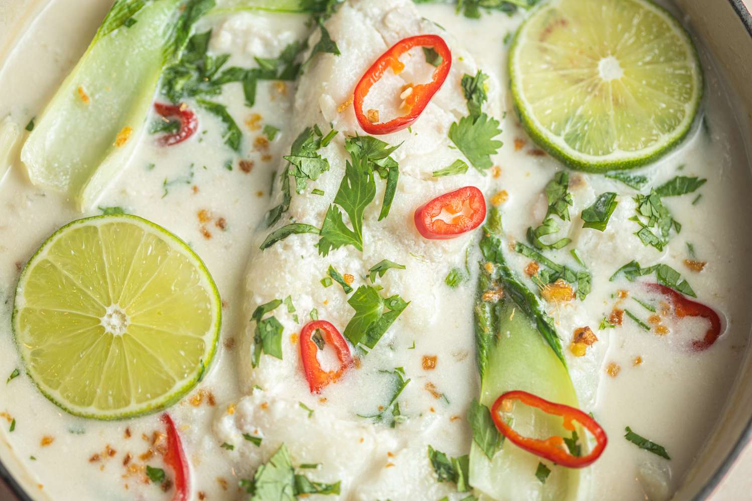 Overhead view of a bowl of Coconut poached fish with bok choy, ginger, and lime.