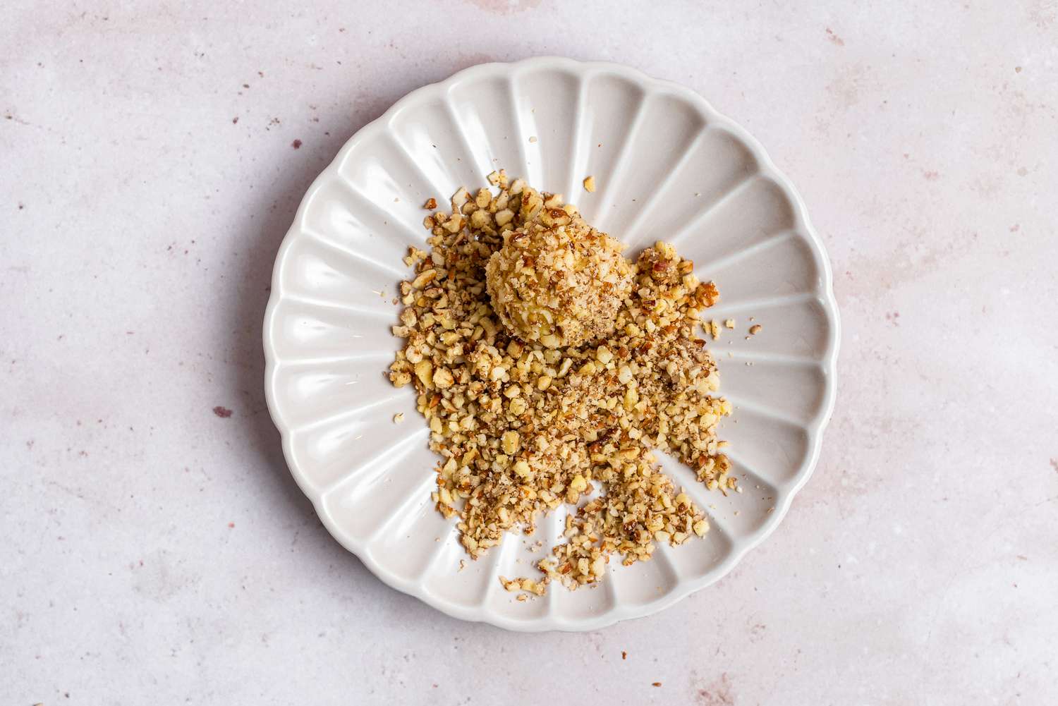 Rolling thumbprint cookie dough ball in nuts.
