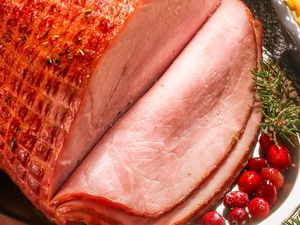 Sliced cooked ham served on a platter with garnishes like cranberries and herbs