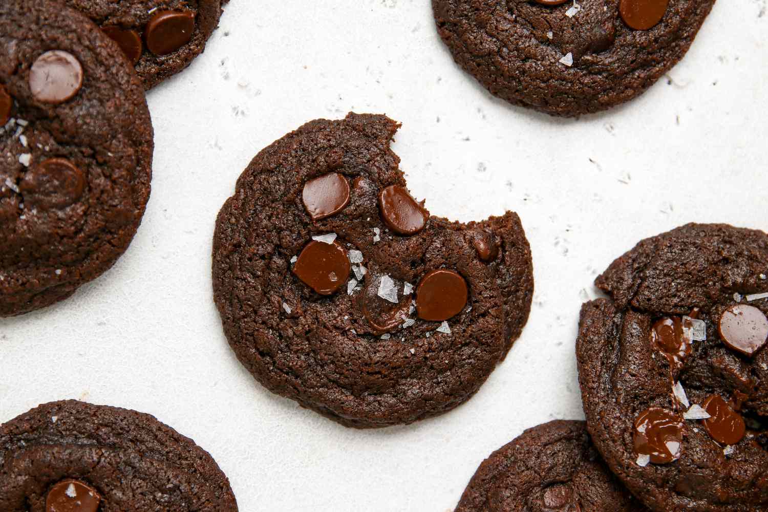 Overhead view of chocolate chip chocolate cookies with the one in the center with a bite removed.
