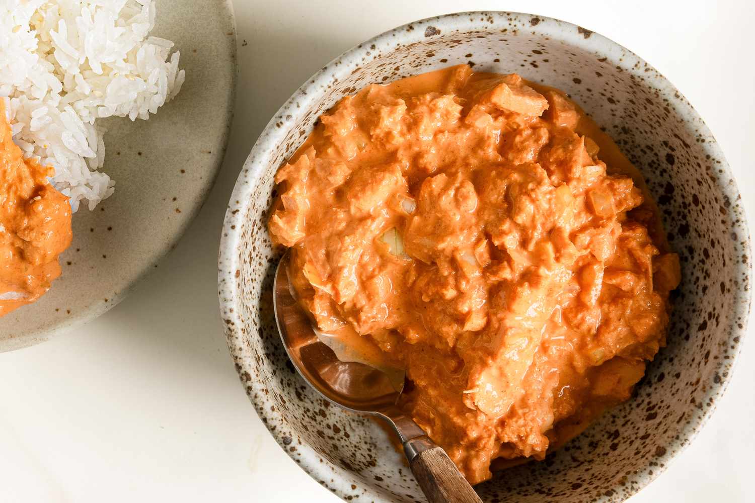 A bowl with spicy tuna salad dish served alongside white rice on a plate