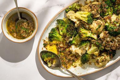 Overhead shot of a bowl with bagna cauda next to a plate with broccoli and cauliflower topped with the condiment