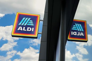 Aldi store signage reflecting on glass, against a background of clouds