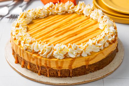 No-bake pumpkin cheesecake on a platter, and in the background, a stack of plates, utensils on the counter, and an orange kitchen towel