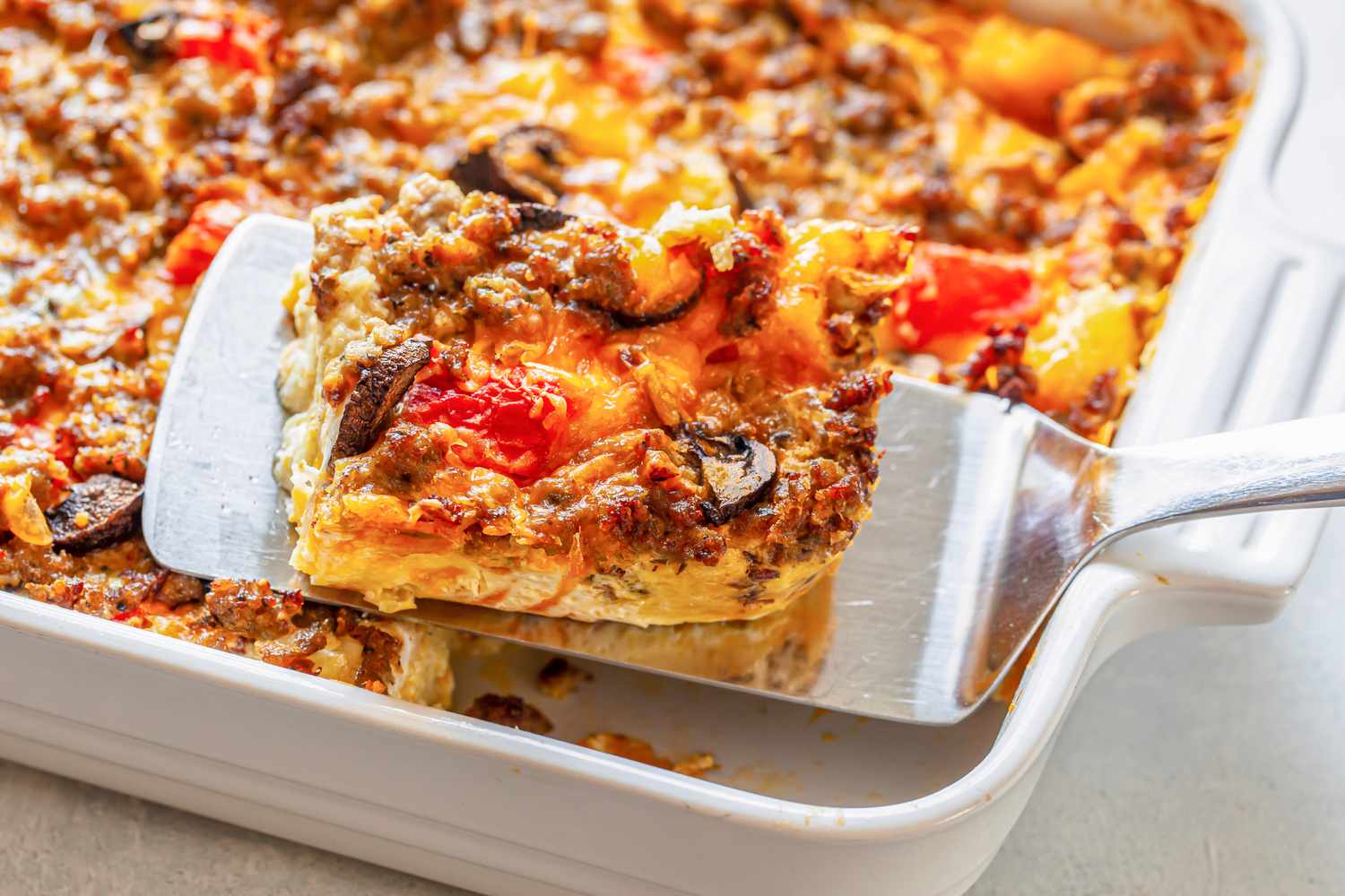 Sausage Breakfast Casserole Lifted from a Casserole Dish Using a Spatula