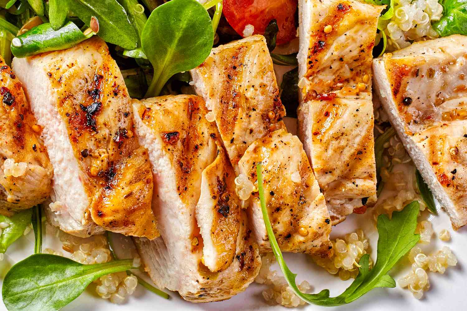 Grilled chicken slices placed on a bed of greens and quinoa
