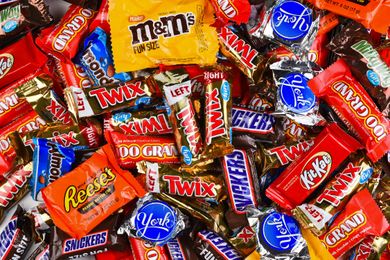 Assorted candies in wrappers including Snickers Twix Reeses and KitKat arranged in a pile