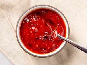 A small bowl filled with sweet and sour sauce, accompanied by a spoon resting on the edge of the bowl