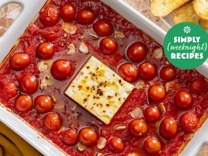 A baked feta dish surrounded by cherry tomatoes in a white baking dish with a Simply Weeknight Recipes logo in the corner