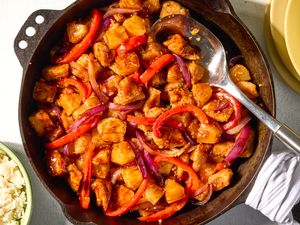 A skillet containing a dish with chunks of chicken pineapple and bell peppers in a sauce