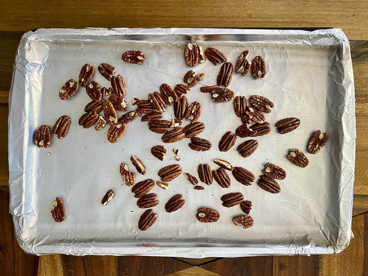 A foil covered baking sheet with whole pecans spread on it to make a Fall Vegetable Salad with Bacon and Maple Dijon Vinaigrette.