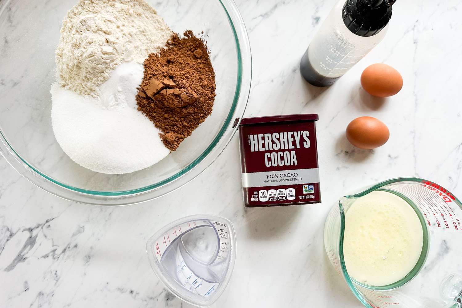 Ingredients for baking including Hersheys Cocoa flour sugar eggs and liquids arranged on a white countertop