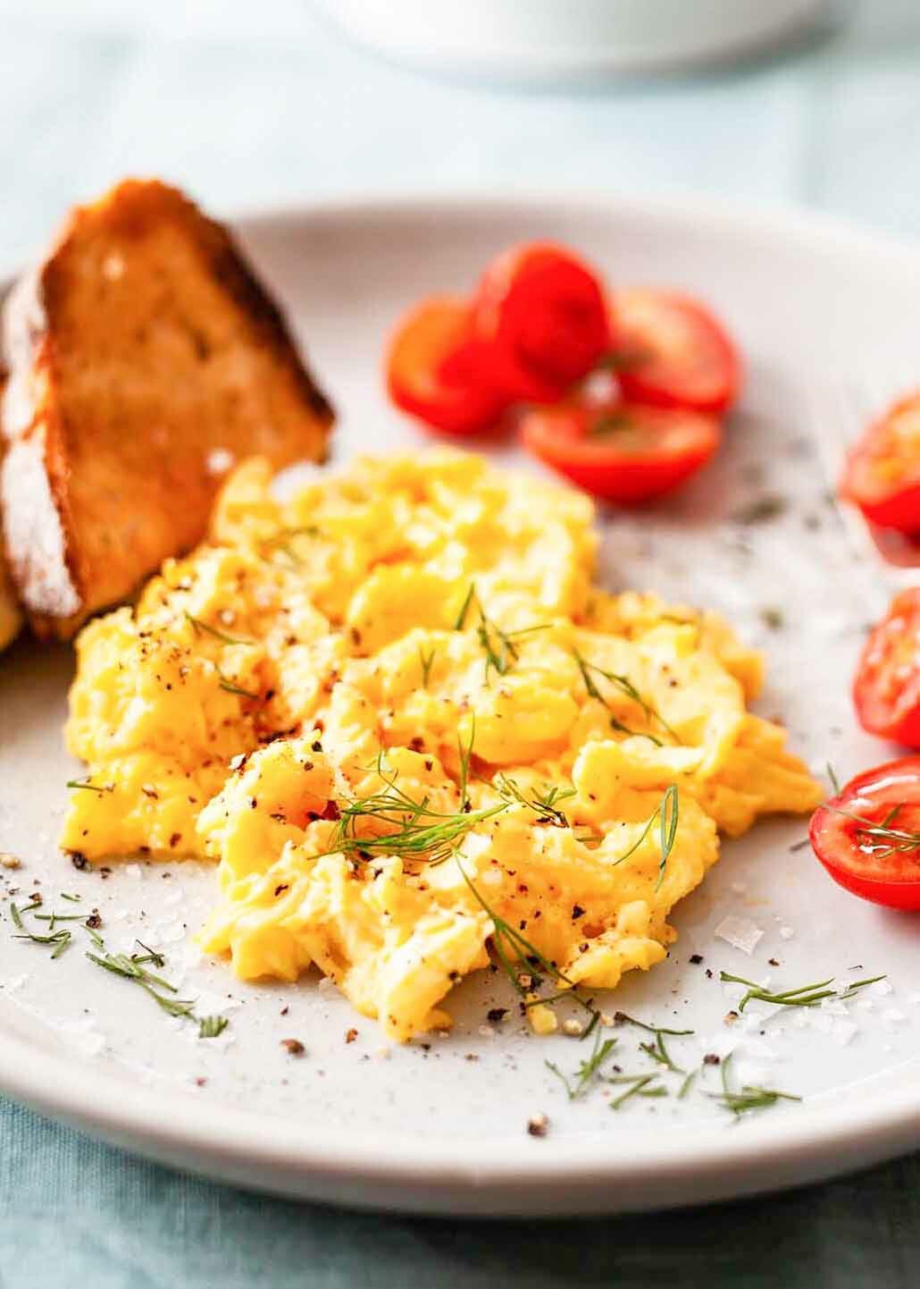 The Best Scrambled Eggs on a plate with toast and tomatoes
