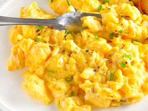 A close up of scrambled eggs on a white plate, garnished with chopped scallion
