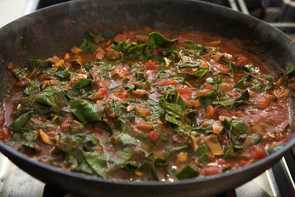 sauce with chard being cooked in skillet for tortellini casserole