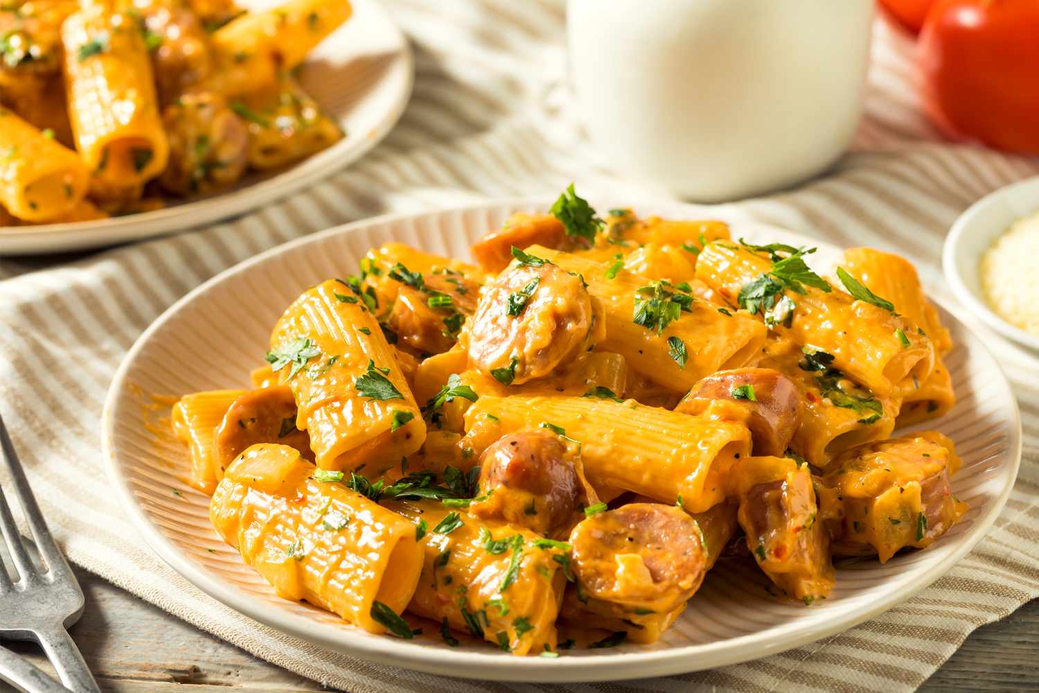 A plate of rigatoni pasta with a creamy tomato sauce and herbs served on a table