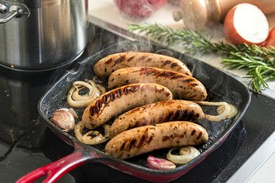 Sausages grilling in a pan with onions and garlic