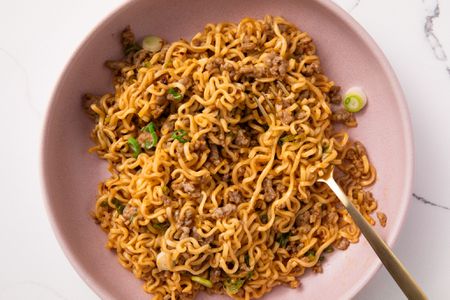 Overhead view of a pink bowl of pork and garlic noodles with a fork and topped with green onions