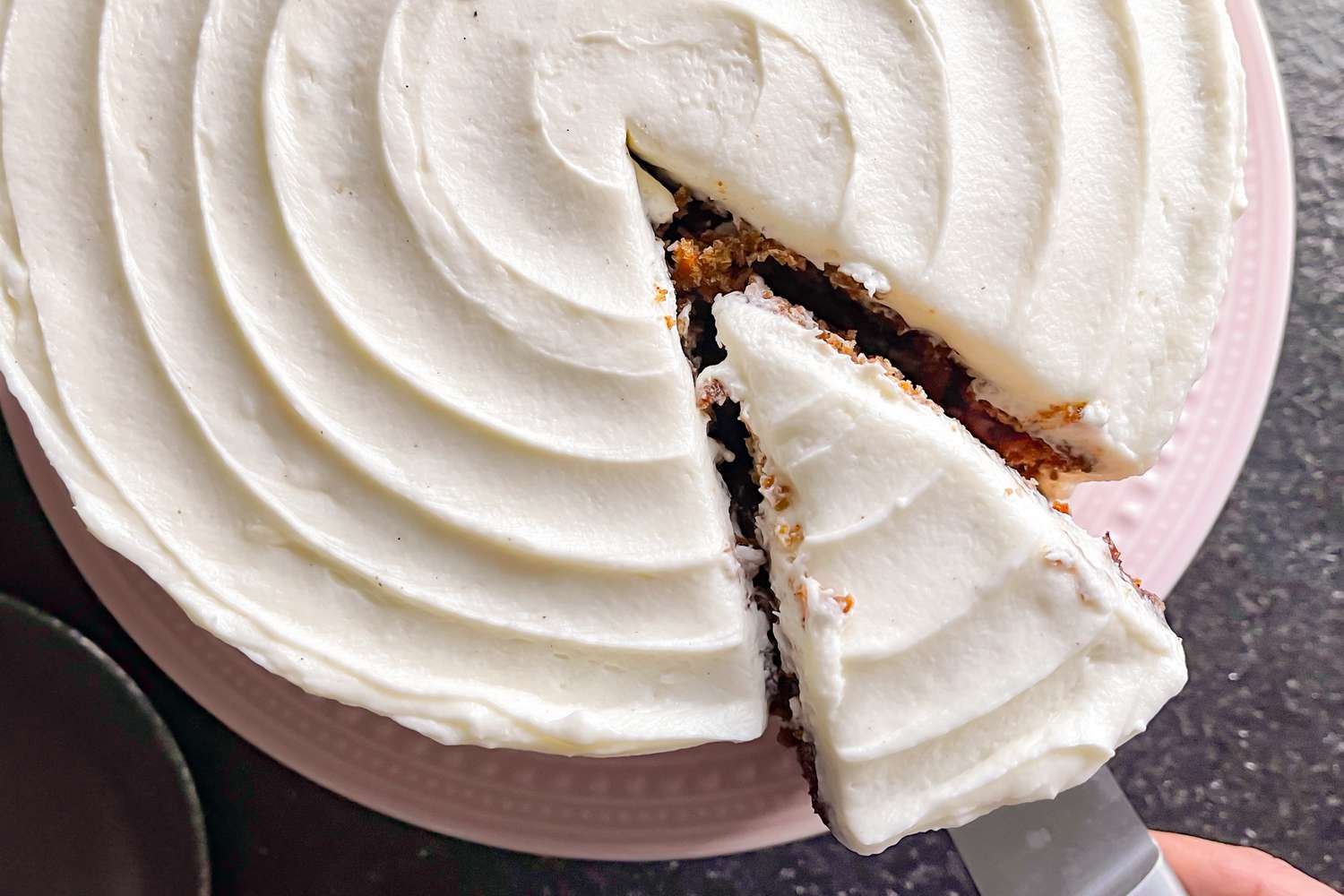 Overhead shot of a carrot cake with a slice being pulled