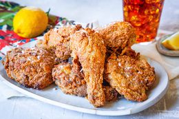 Sweet Tea Fried Chicken on a Platter, and in the Surroundings, a Glass of Ice Tea, a Lemon Wedge on a Small Saucer, and a Lemon on a Colorful Kitchen Towel