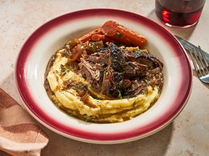 A serving bowl of pot roast over mashed potatoes with carrots on the side