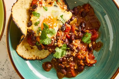 A closeup of a bowl with a serving of the black bean and egg bake recipe served with a corn tortilla, garnished with fresh cilantro