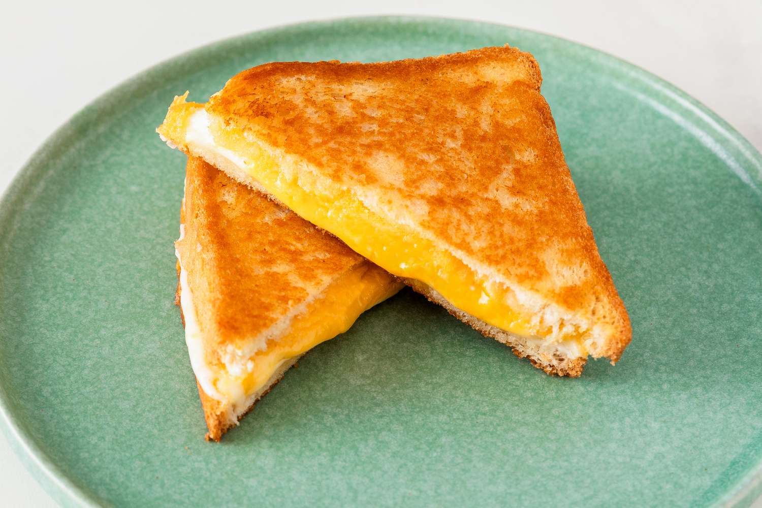 Two halves of a grilled cheese sandwich on a light green plate