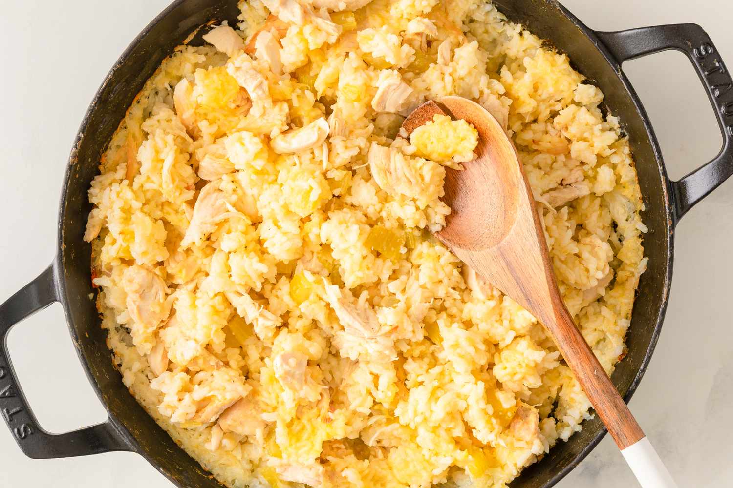 A pan of rice mixed with shredded chicken and a wooden spoon arranged freshly cooked