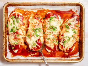 Overhead view of a baking sheet of four bbq baked chicken breasts topped with cheese and green onions on parchment paper