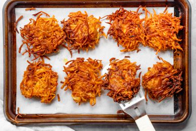 Sweet Potato Latkes on a Parchment Lined Baking Sheet with One on a Spatula