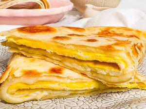 Folded egg tortilla on a patterned plate, layered with melted cheese, served with a dish in the background.